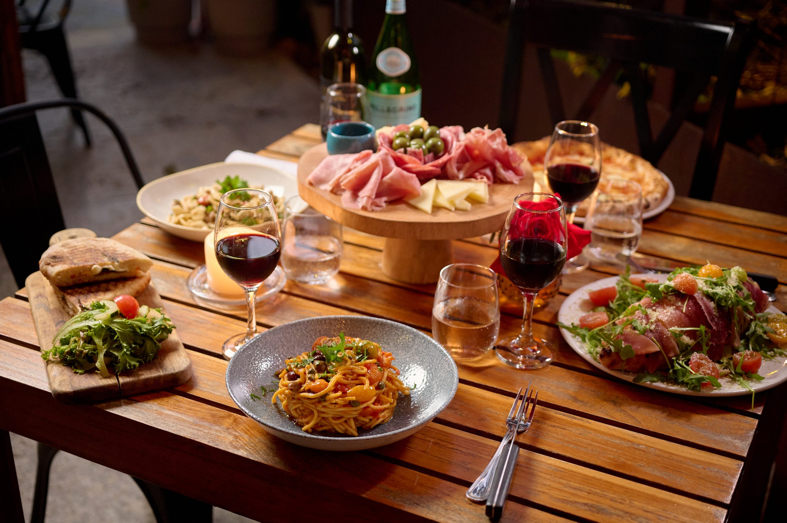 A table at Ironside Pizza, family style restaurant in Miami adorned with plates of Italian food and glasses of wine.